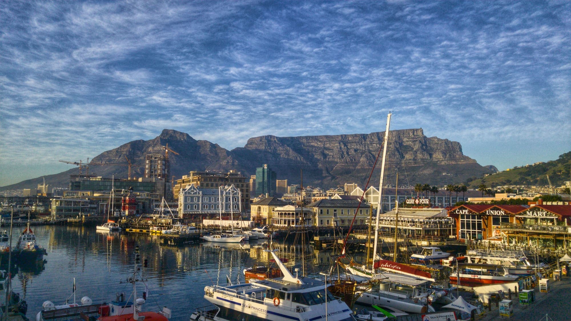 O porto do V&A Waterfront, na Cidade do Cabo, com barcos atracados e a Table Mountain ao fundo.