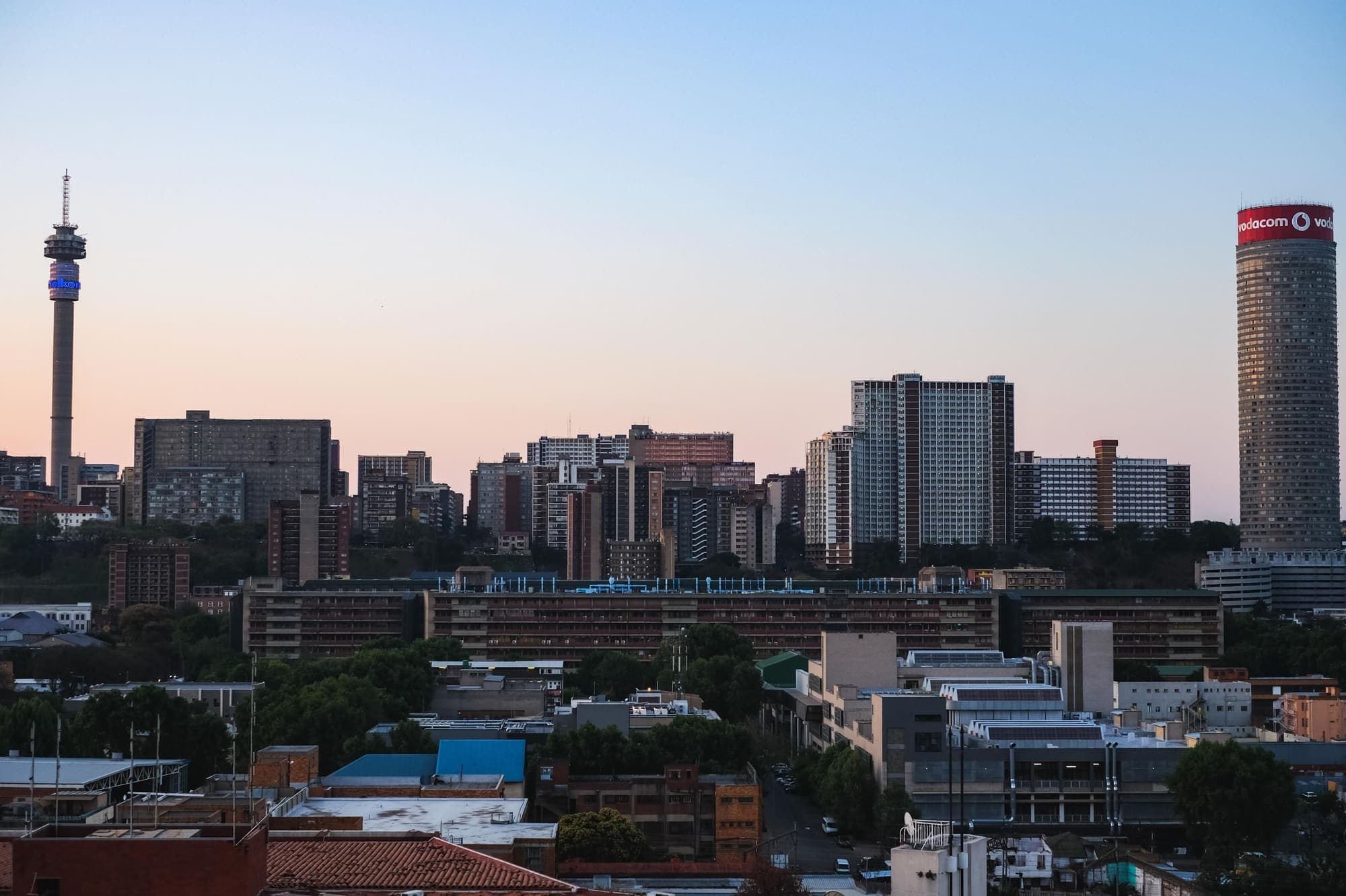 O centro de Joanesburgo ao entardecer, com a torre de Hillbrow à esquerda e o cilindro da Ponte Tower à direita.