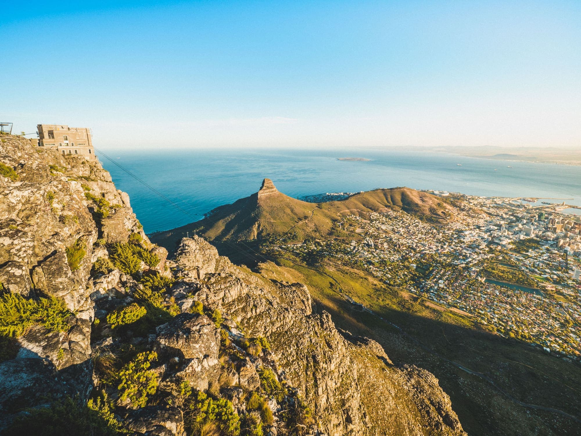 Vista do alto da Table Mountain, com a estação do teleférico à esquerda e, abaixo, o Lion's Head e a Cidade do Cabo à beira do mar.