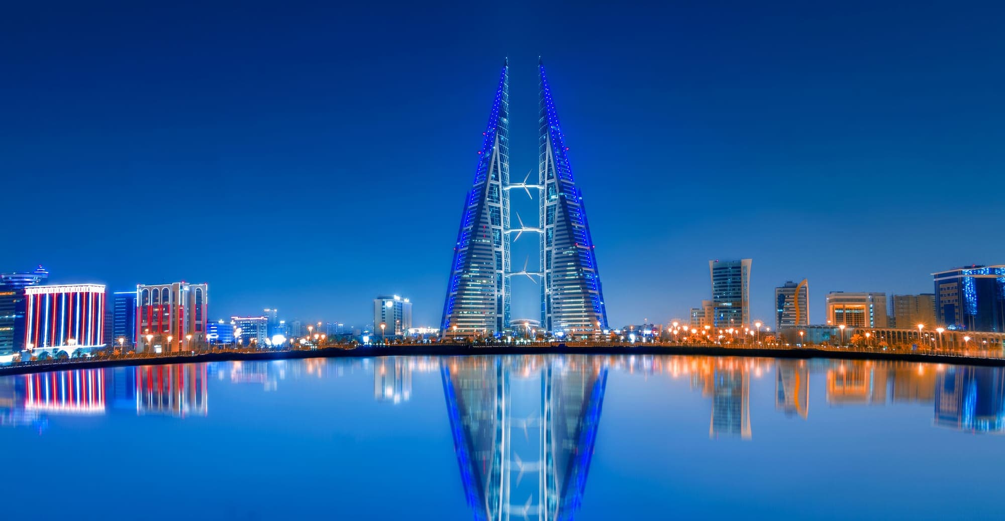 O Bahrain World Trade Center, em Manama, iluminado de azul ao anoitecer e refletido na água.