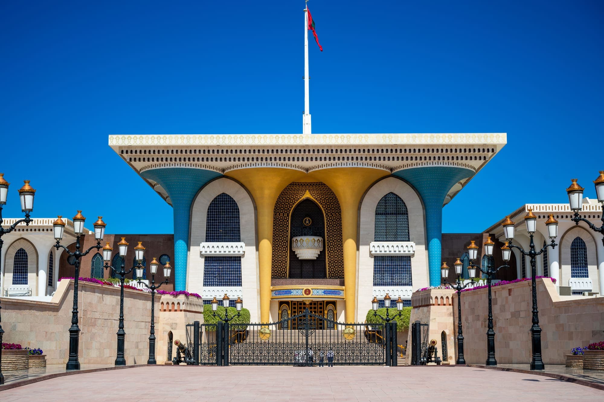 A fachada do Palácio Al Alam, em Mascate, com colunas azuis e douradas e a bandeira de Omã no mastro.