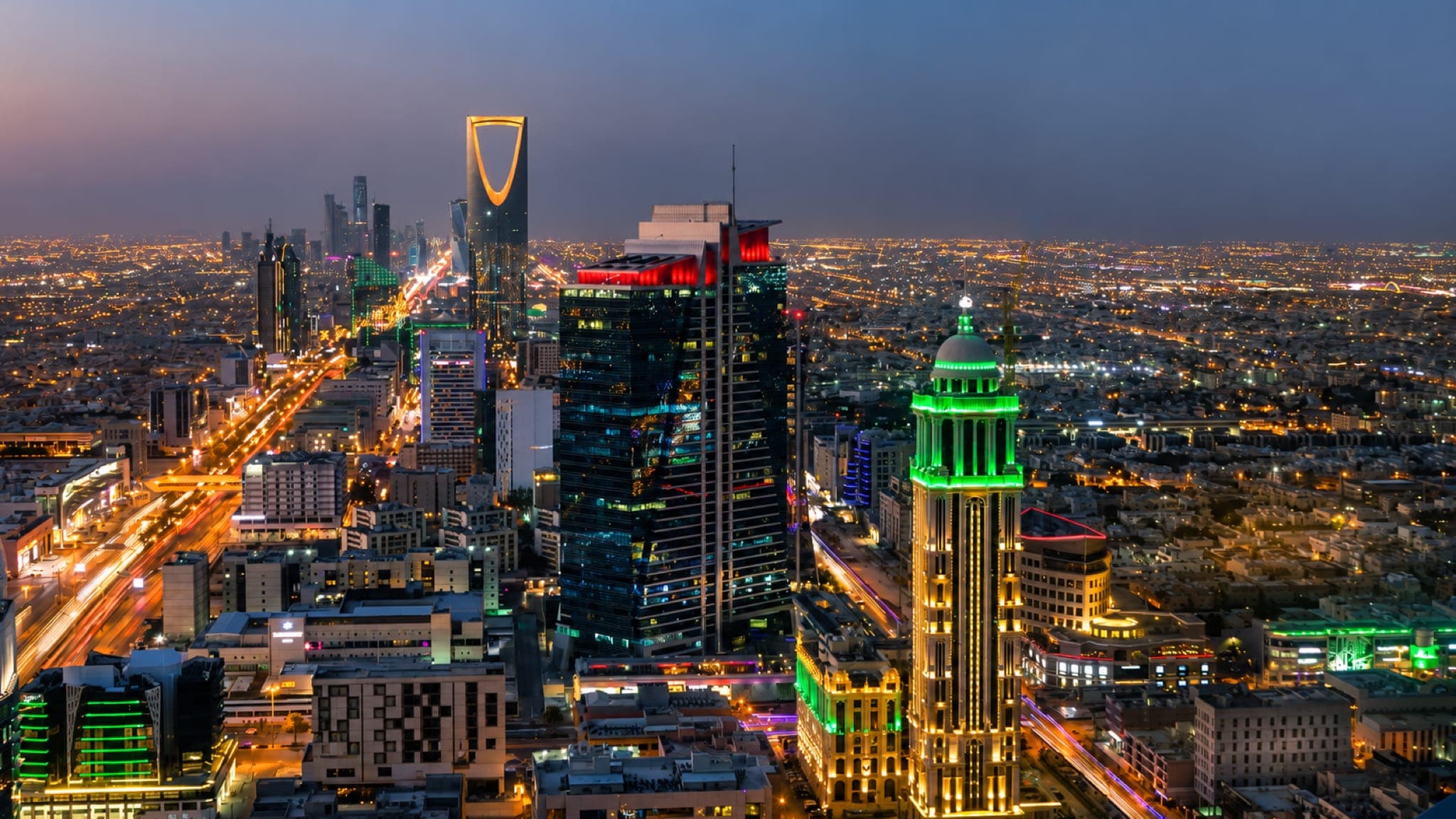 Riade ao anoitecer, com o Kingdom Centre iluminado entre os prédios e as luzes da cidade até o horizonte.