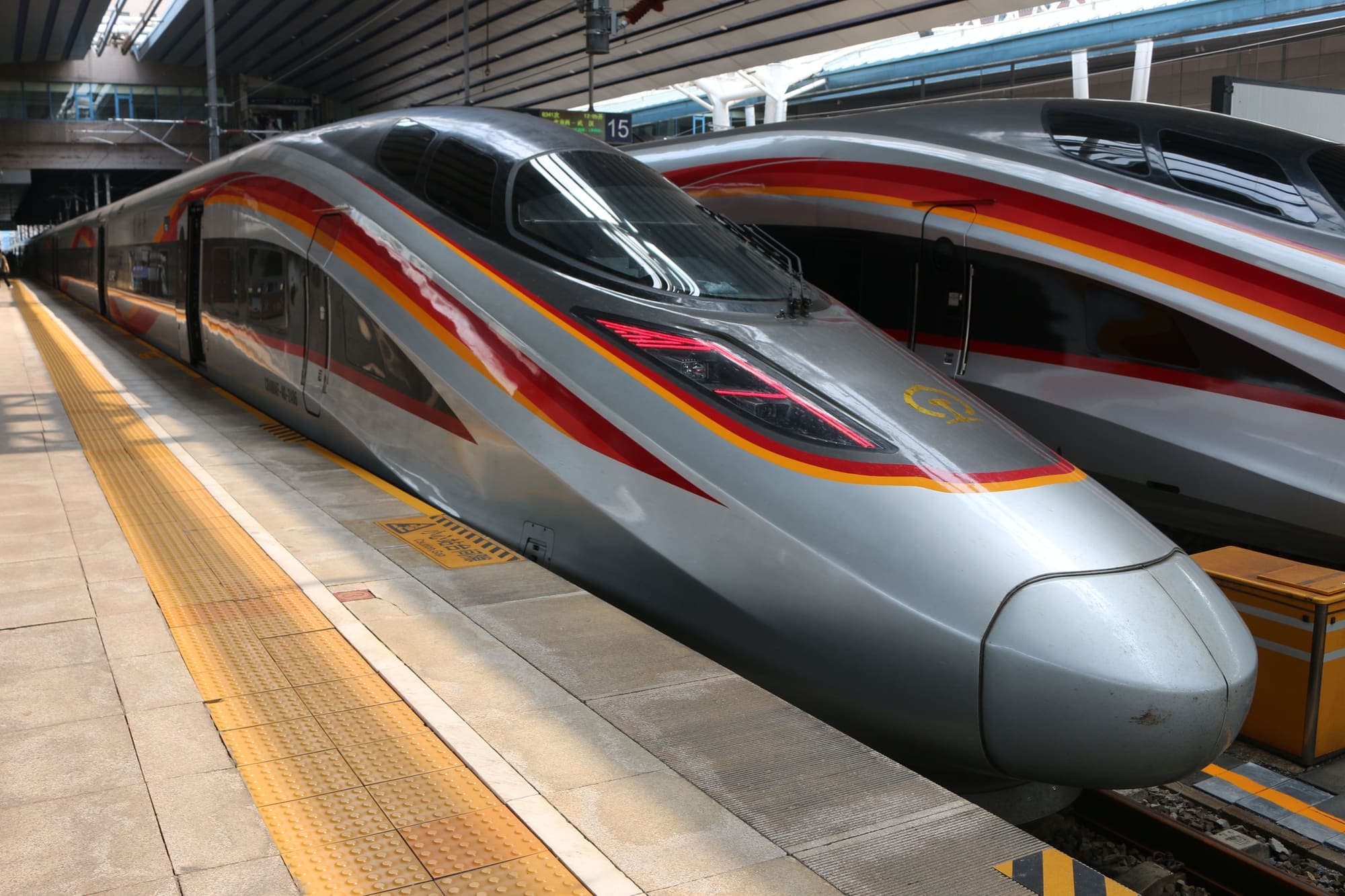 Trem-bala chinês, prateado com faixas vermelhas, parado na plataforma de uma estação em Pequim.