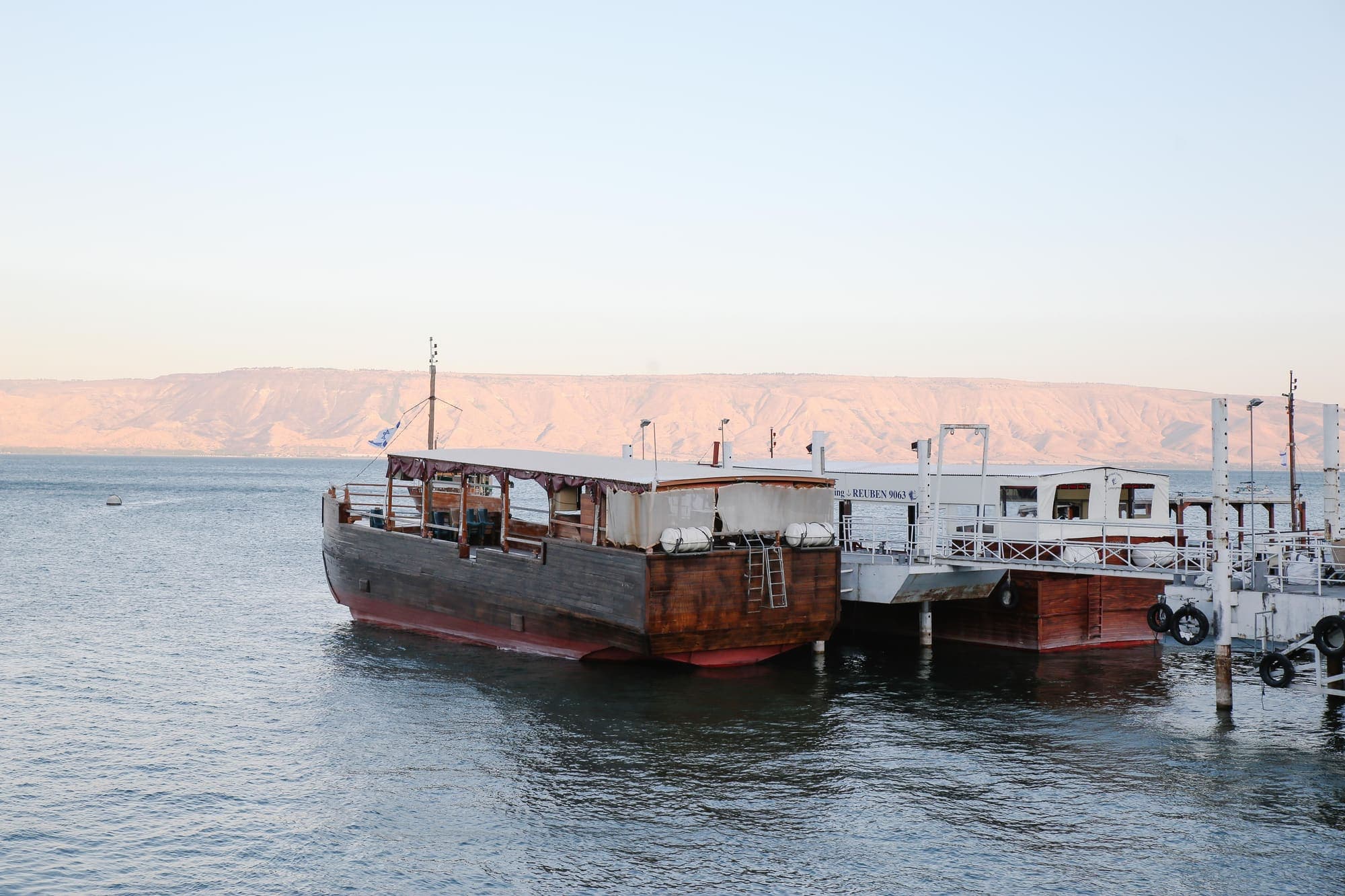Barcos de madeira atracados no Mar da Galileia, com as colinas da outra margem ao fundo.