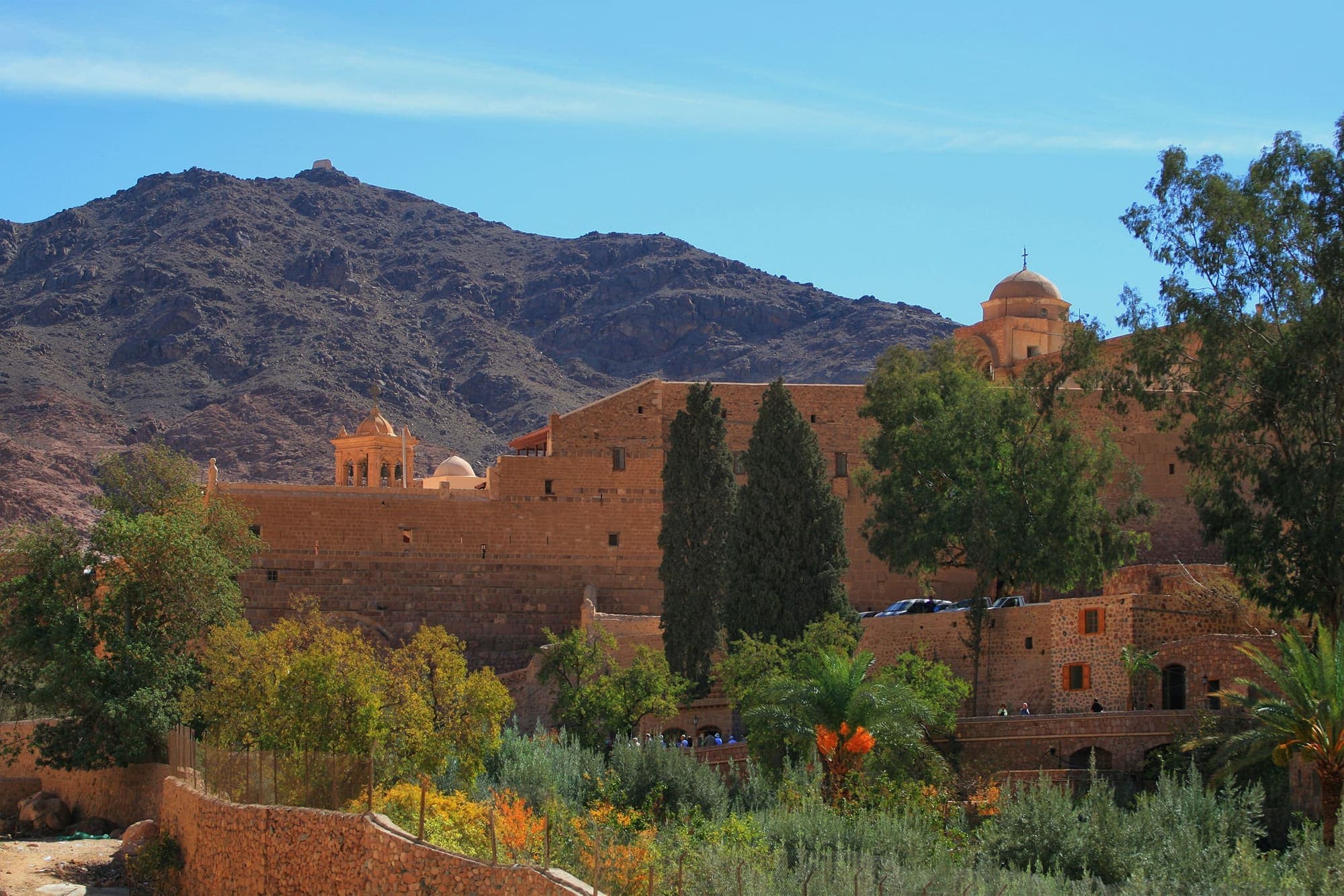 O Mosteiro de Santa Catarina, ao pé do Monte Sinai, com suas muralhas de pedra entre árvores e as montanhas do deserto ao fundo.