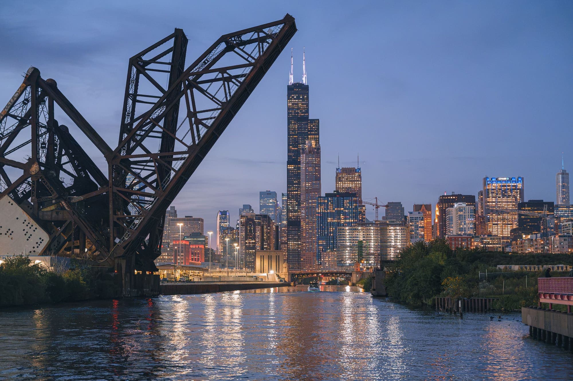 A Willis Tower e os arranha-céus de Chicago ao entardecer, vistos do Rio Chicago, com uma antiga ponte ferroviária levadiça erguida à esquerda.