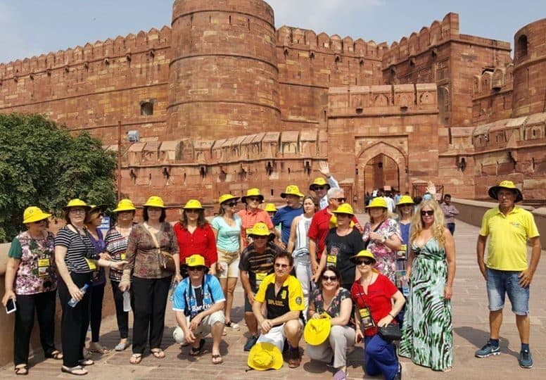 Grupo da Leão Viagens com chapéus amarelos diante das muralhas de arenito vermelho de um forte na Índia.