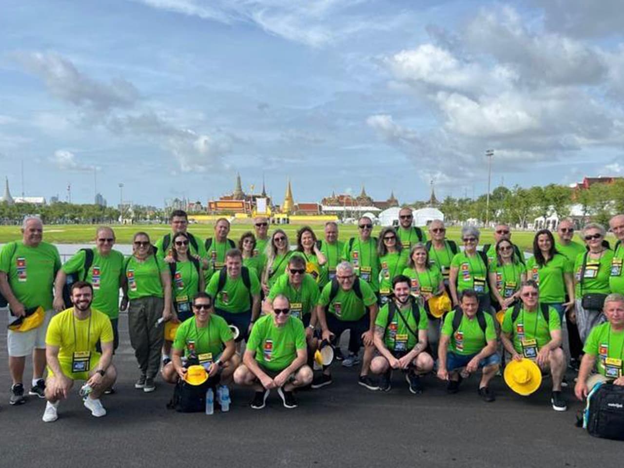Grupo Cotrijal, de camisas verdes e chapéus amarelos, numa praça com os telhados dourados de um palácio tailandês ao fundo.
