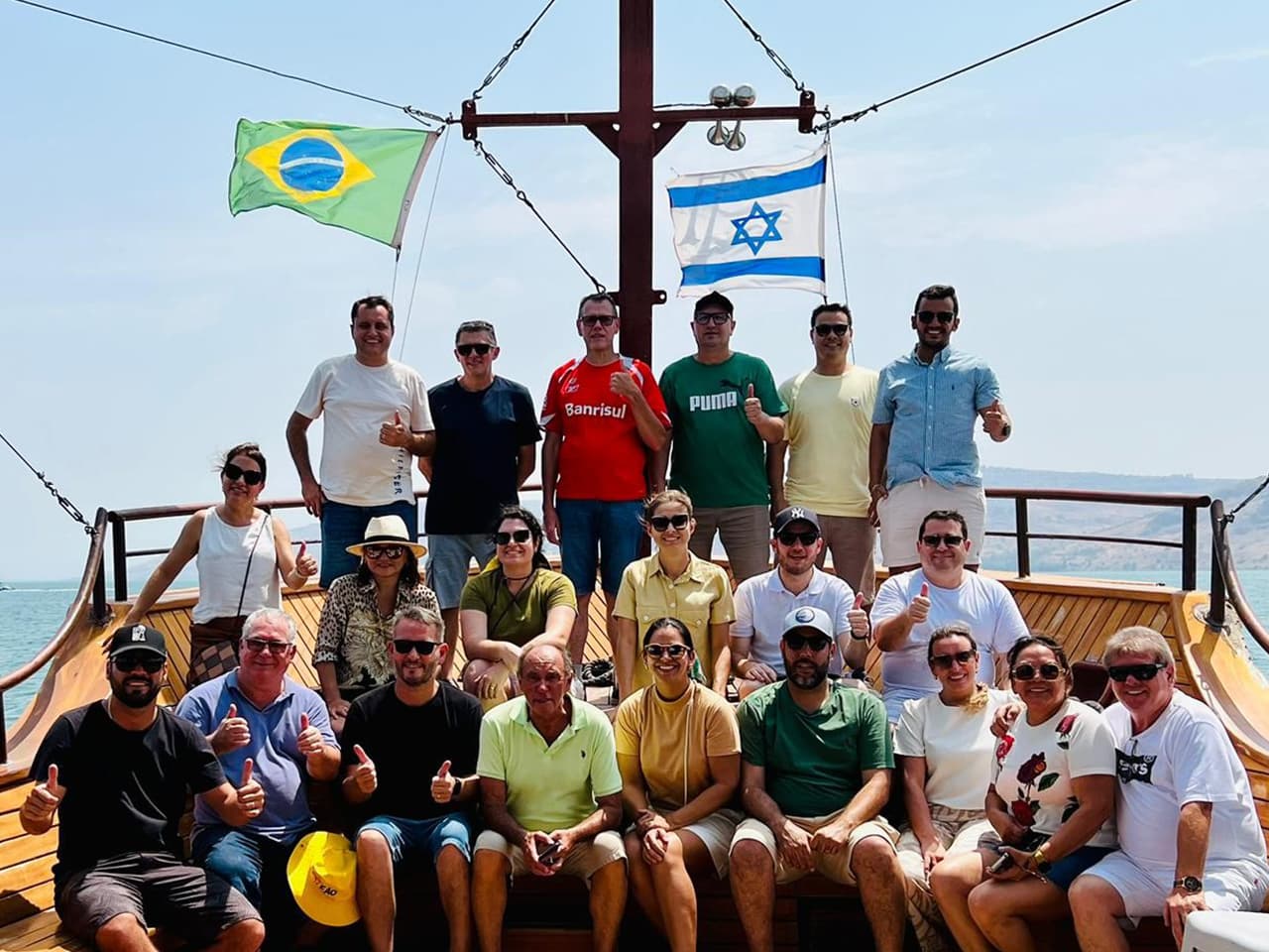 Grupo Adama num barco de madeira no Mar da Galileia, com as bandeiras do Brasil e de Israel no mastro.