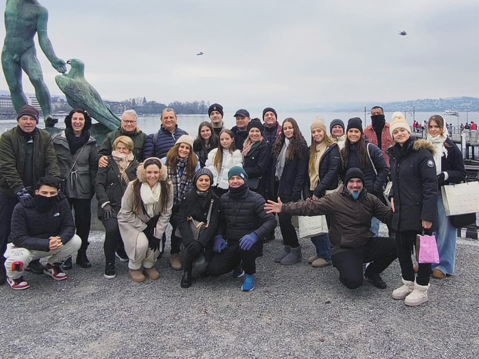 Grupo da Leão Viagens, de casacos de inverno, à beira de um lago, ao lado de uma estátua de bronze.