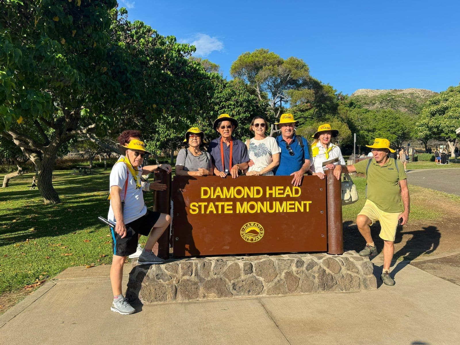 Grupo da Leão Viagens com chapéus amarelos atrás da placa do Diamond Head State Monument, no Havaí.