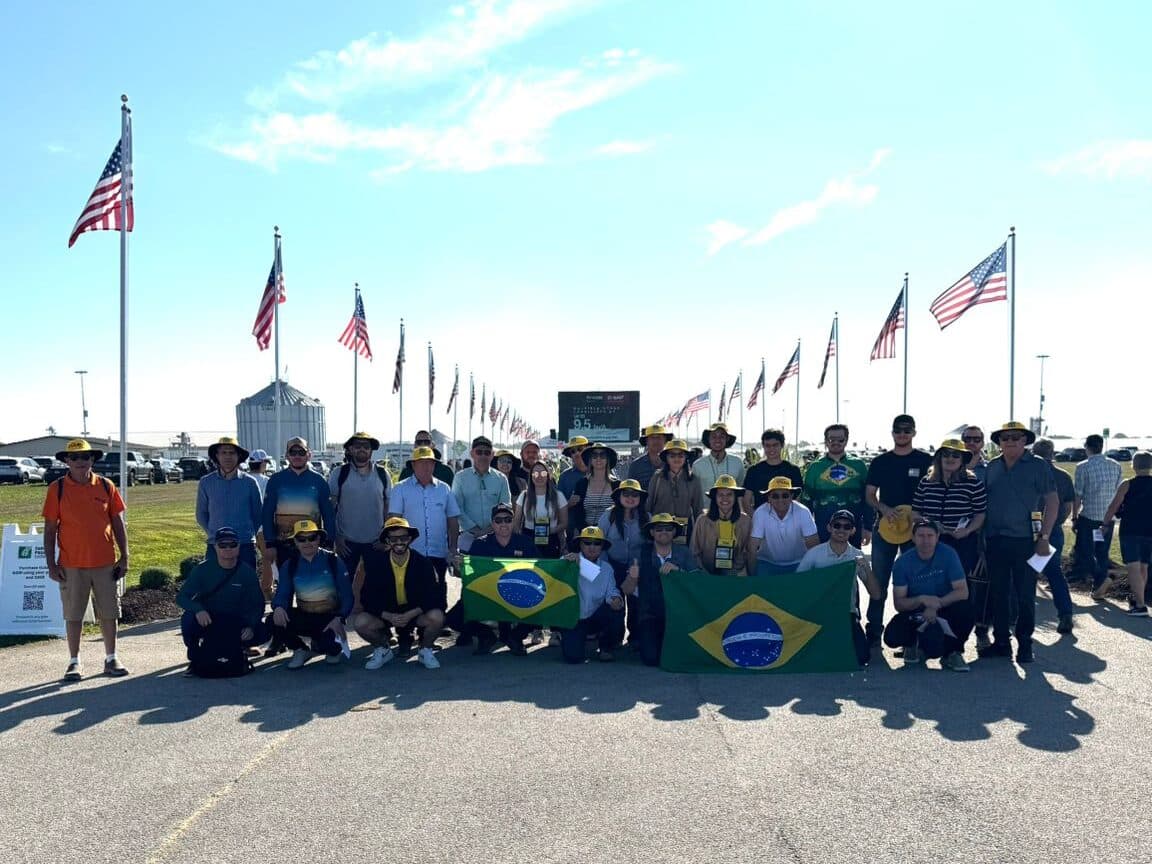 Grupo da Leão Viagens com chapéus amarelos e duas bandeiras do Brasil na avenida de bandeiras americanas da Farm Progress Show.