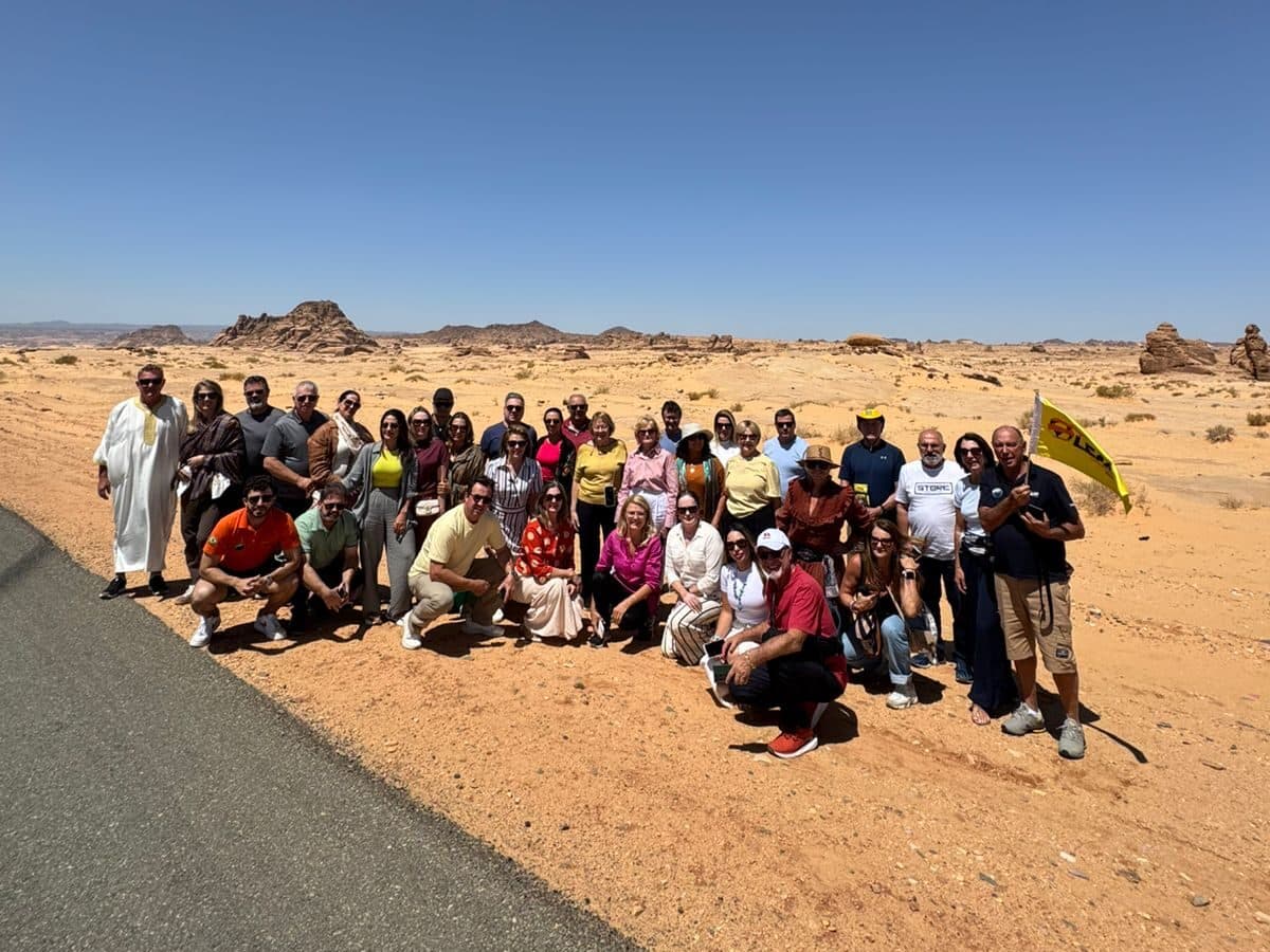 Grupo da Leão Viagens à beira de uma estrada no deserto, entre formações de arenito, com a bandeira amarela da Leão.